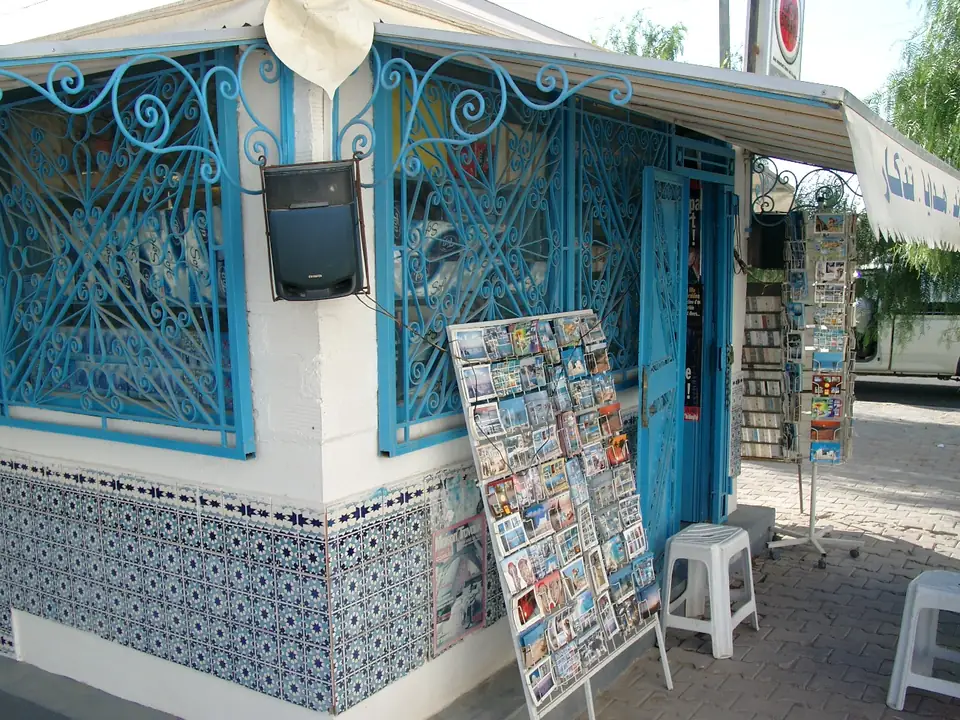 Weißer Kiosk mit blauem Schmiedegitter und einem Postkartenständer