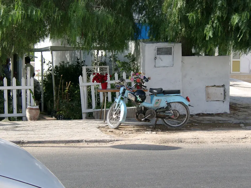 Moped vor einem weißen Gartenzaun und einem kleinen Blumenverkauf