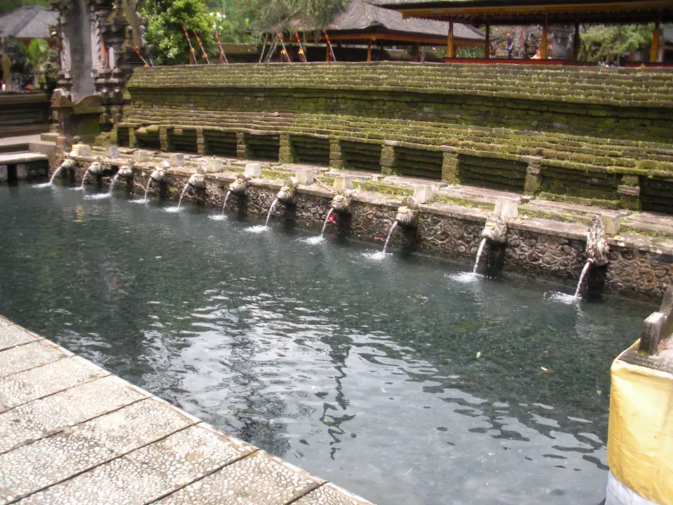 Steinernes Badebecken mit einer Reihe von Wasserspeiern, an denen Gläubige stehen