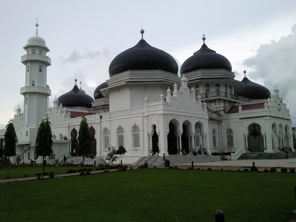 Weiße Moschee mit schwarzen Kuppeln und Minarett vor blauem Himmel