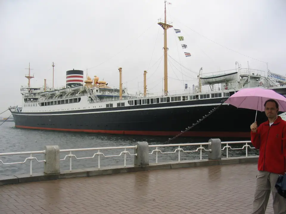 Reisender mit rosa Regenschirm vor dem schwarzen Passagierschiff Hikawa Maru