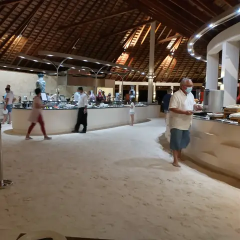 Offener Restaurantbereich mit hohem Holzdach, Sandboden und Buffetstationen