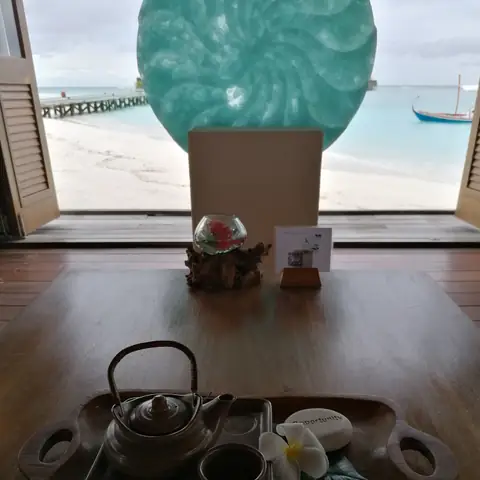 Teetablett mit Kanne, Tasse und Blüte vor einem offenen Fenster mit Blick auf Strand und Lagune