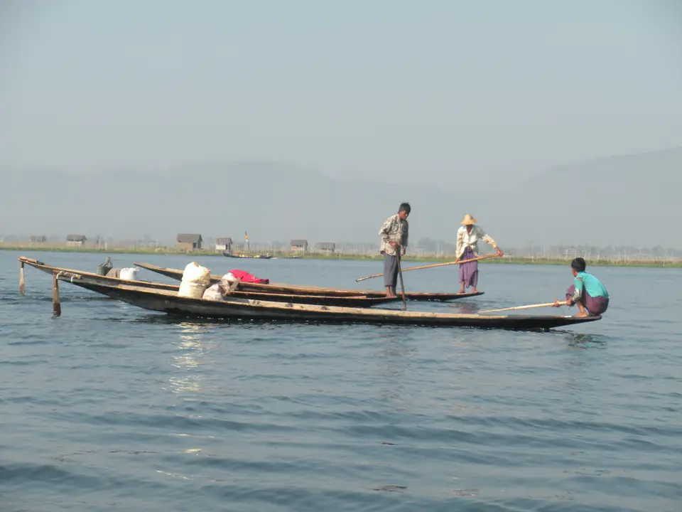 Drei Menschen in schmalen Holzbooten auf dem Inle-See vor Bergen im Dunst