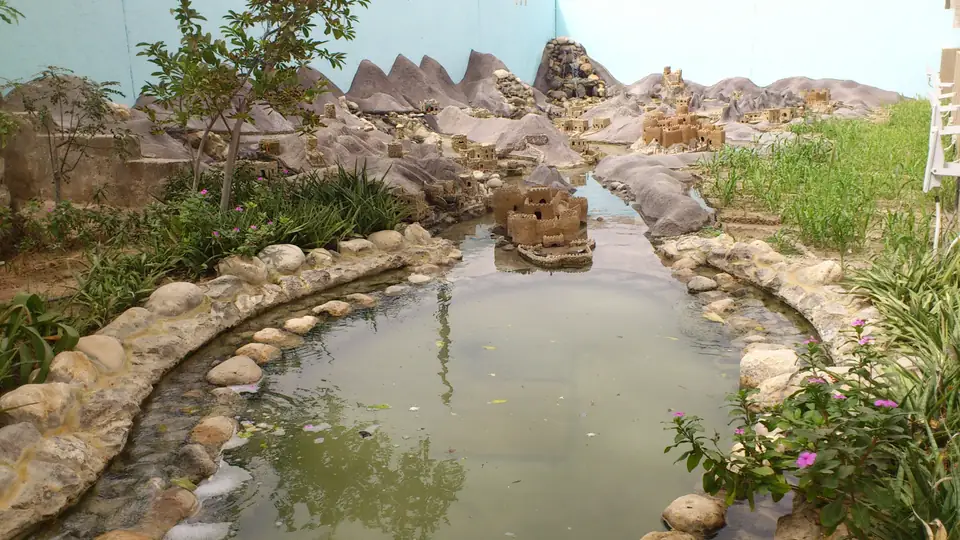 Miniaturdorf mit Lehmfestung und Wasserlauf im begrünten Museumsgarten