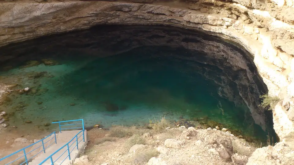 Türkisfarbenes Wasser in einem tiefen Kalksteinbecken mit Treppe und blauem Geländer