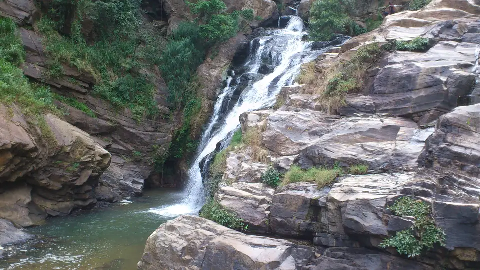 Wasserfall über gestufte Felsen in ein grünliches Becken, umgeben von tropischer Vegetation