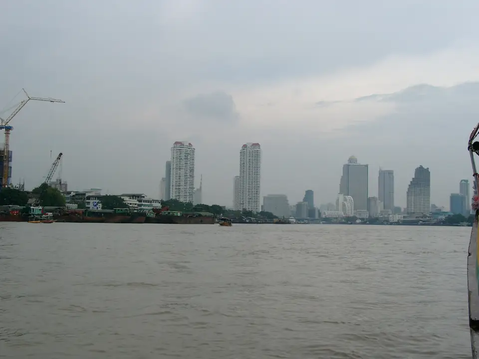 Blick über einen breiten Fluss auf Bangkoks Uferbebauung