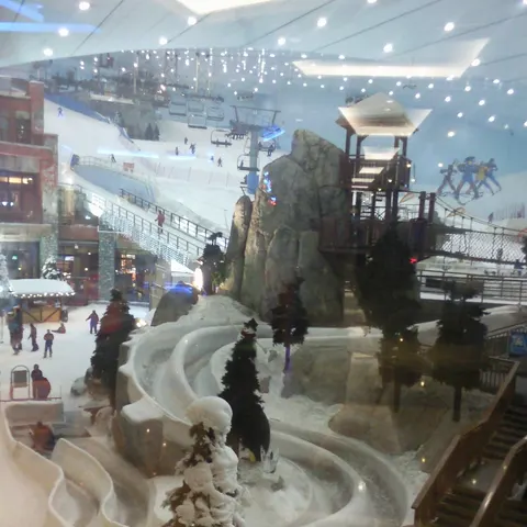 Blick durch die Scheibe in die Skihalle von Ski Dubai mit schneebedeckter Piste, Sessellift und verschneiten Bäumen