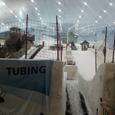 Tubing-Bahn in Ski Dubai zwischen Schneewänden und Schutznetzen, mit der Skipiste im Hintergrund