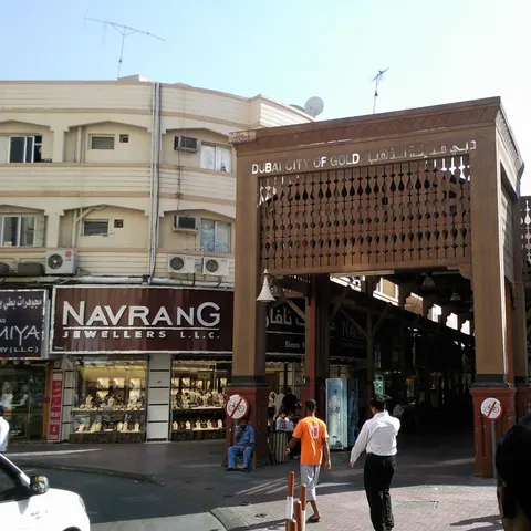 Hölzernes Eingangstor zum Deira Gold Souk mit der Aufschrift „Dubai City of Gold“ neben einem Schmuckgeschäft