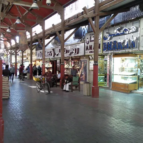 Reihe von Schmuckgeschäften unter dem Holzdach des Deira Gold Souk mit Passanten und einem Mann mit Fahrrad