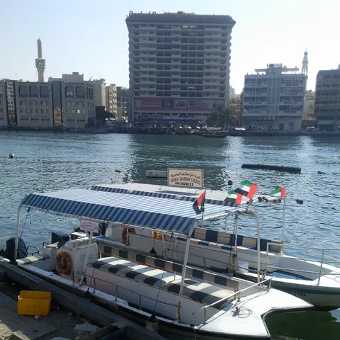 Vertäute Ausflugsboote mit gestreiften Sonnendächern und Emirate-Flaggen am Dubai Creek