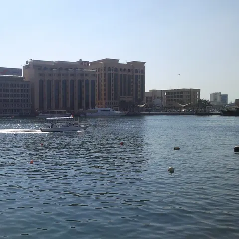 Ein überdachtes Motorboot fährt über den Dubai Creek vor den Gebäuden am gegenüberliegenden Ufer
