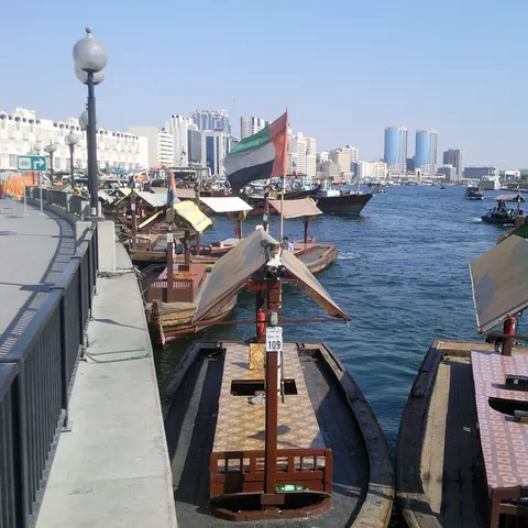 Traditionelle hölzerne Abras liegen am Ufer des Dubai Creek, weitere Boote fahren über den Meeresarm