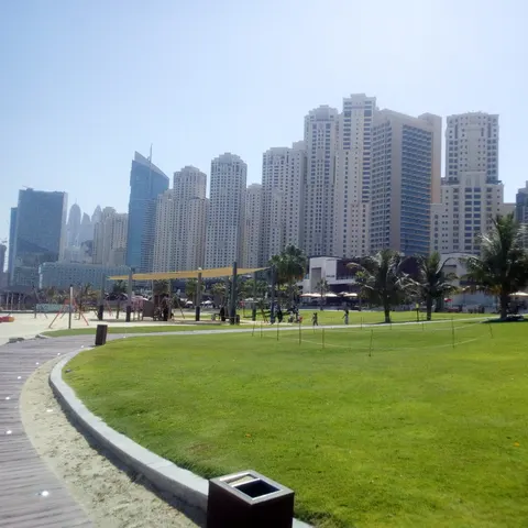 Grüne Rasenfläche mit Palmen und Spielbereich bei The Beach vor den Hochhäusern der Jumeirah Beach Residence