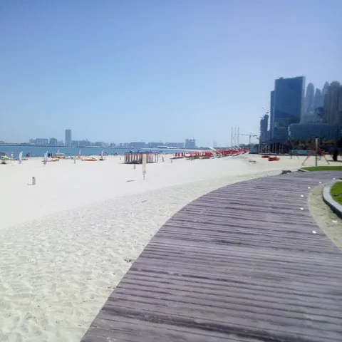 Geschwungener Holzweg entlang des breiten Sandstrands bei The Beach mit Wassersportbooten am Meer