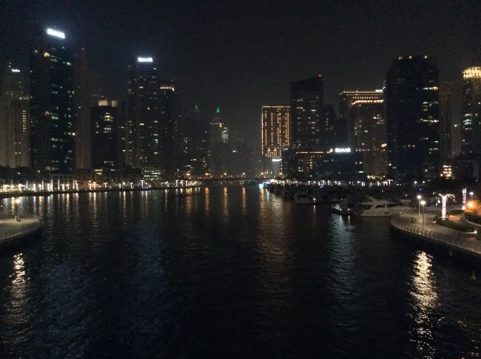 Beleuchtete Hochhäuser und Yachten an der Dubai Marina bei Nacht mit Spiegelungen auf dem Wasser