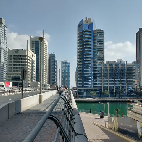 Blick von einer Brücke auf den Kanal der Dubai Marina mit Uferpromenade und gläsernen Hochhäusern