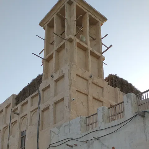 Sandfarbenes Gebäude mit Windturm, Holztüren, Laternen und einer Lichterkette in Al Seef am Dubai Creek