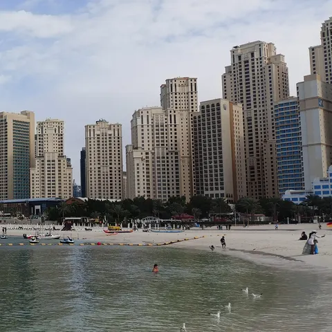 Blick vom Wasser auf den Strand bei The Beach mit Jetskis, Badegästen und den Hochhäusern der Jumeirah Beach Residence