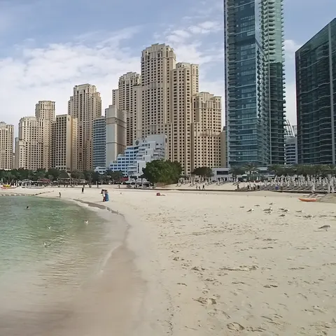 Geschwungene Uferlinie am JBR-Strand mit klarem Wasser, Möwen und einer dichten Reihe von Hochhäusern