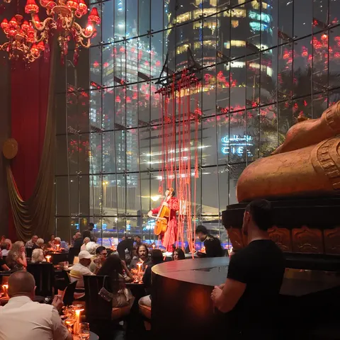 Cellistin in Rot vor der hohen Fensterfront der Buddha-Bar Dubai, mit roten Kronleuchtern und Gästen an den Tischen