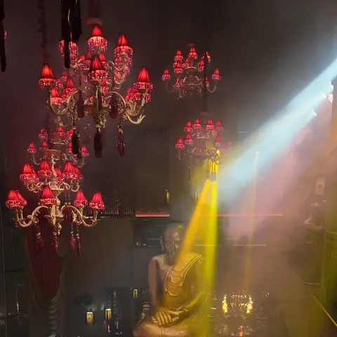 Blick von der Galerie auf die goldene Buddha-Statue, rote Kronleuchter und den Restaurantbereich im Licht der Show