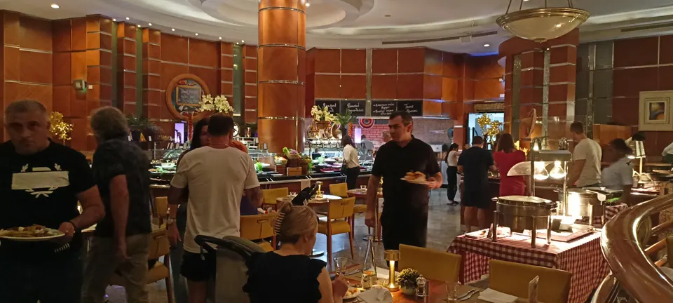 Gäste zwischen den Buffetstationen in einem Restaurant mit rotbraunen Säulen und dicht stehenden Tischen
