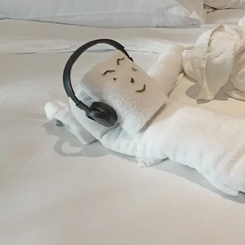 Liegende Handtuchfigur mit Kopfhörern neben einer aufgerichteten Tierfigur auf dem Hotelbett