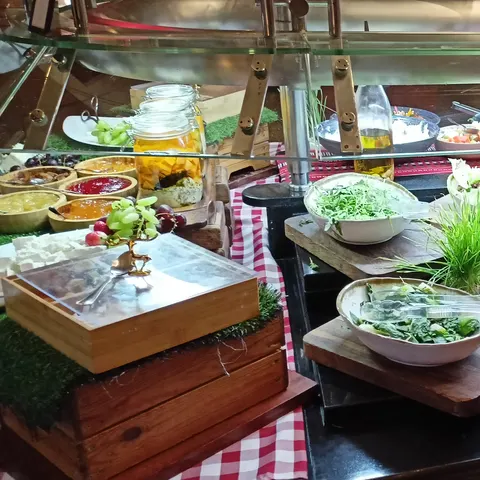 Salatbar mit Gurken, Blattsalaten und weiteren Zutaten in weißen Schüsseln auf Holzbrettern