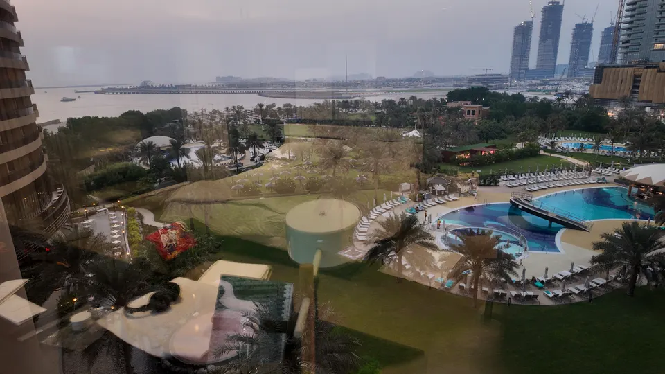 Blick durch das Zimmerfenster über die weitläufige Gartenanlage des Le Royal Méridien mit Rasenflächen, Palmen, Liegen und mehreren Pools zum Strand und Meer
