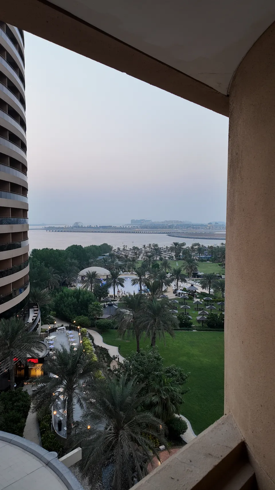 Blick aus der tiefen Balkonnische des Le Royal Méridien über Palmen, Garten und Pool zum Meer, seitlich von Hotelwand und Nachbargebäude eingerahmt