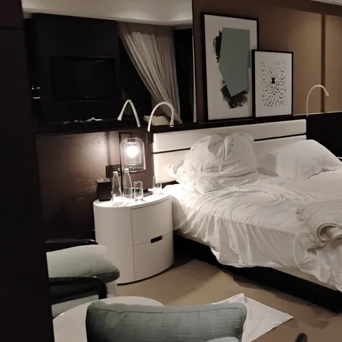 Doppelbett mit weißer Bettwäsche, Nachttisch, Leselampen und Bildern vor einer dunklen Holzwand im Le Royal Méridien