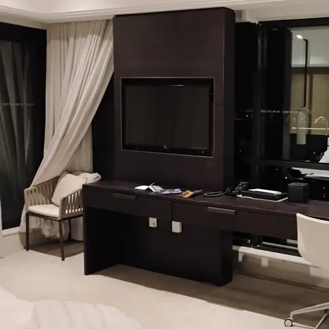 Langer dunkler Schreibtisch mit Telefon, Lampe und weißem Stuhl sowie Fernseher und Sitzgelegenheiten im Hotelzimmer