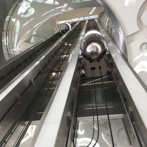 Blick nach oben entlang der gläsernen Aufzugsschächte in der weißen Eingangshalle