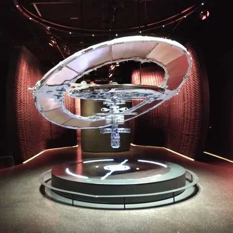 Beleuchtetes ringförmiges Raumstationsmodell auf einem runden Sockel in einem dunklen Ausstellungsraum