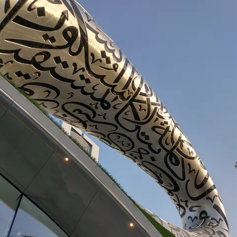 Geschwungene silberne Fassade mit arabischen Schriftzeichen über dem verglasten Sockel des Museums