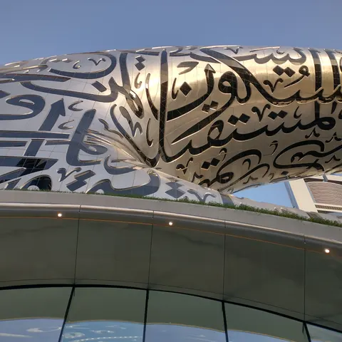 Blick von unten auf die ringförmige Fassade mit arabischer Kalligrafie vor blauem Himmel