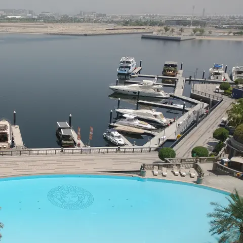 Blick von oben auf den türkisfarbenen Pool mit Medusa-Mosaik und die Boote am Anleger im Dubai Creek