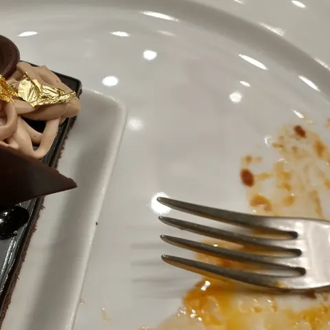 Dunkles Schokoladendessert mit aufgesetzter Creme, Schokoladendekoration und Blattgold auf einem weißen Teller