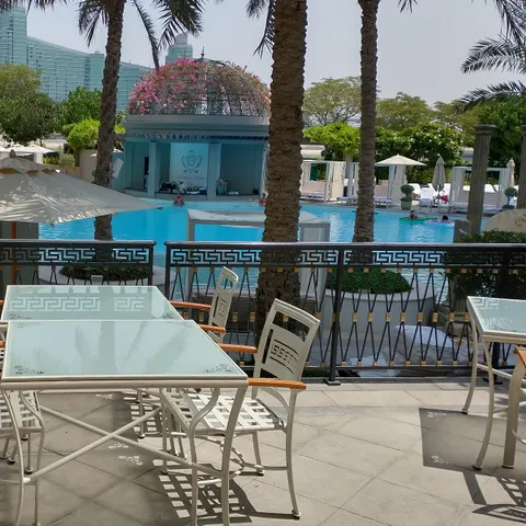 Tische und Stühle hinter einem Geländer mit Mäandermuster vor einem von Palmen umgebenen Pool