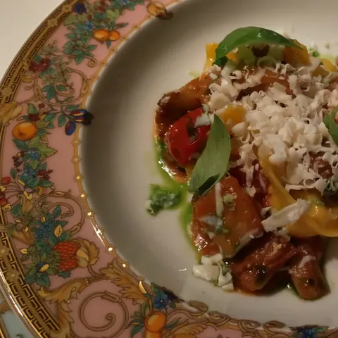 Tortellini mit Tomaten, Basilikum und geriebenem Käse auf einem floral verzierten Versace-Teller