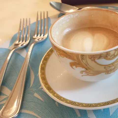 Kaffee in einer goldfarben verzierten Tasse auf einer passenden Untertasse vor dem Besteck