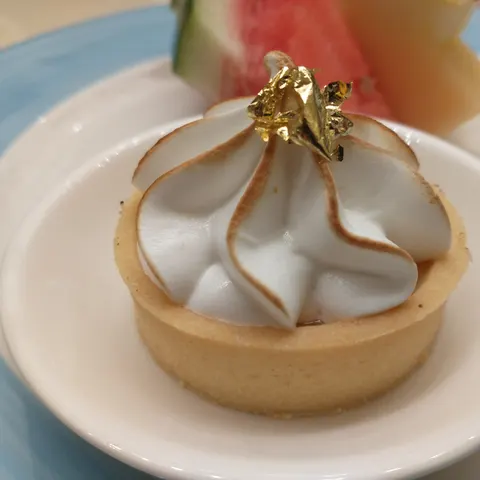 Kleine Tarte mit gebräunter Baiserhaube und Blattgold, daneben Melonenstücke