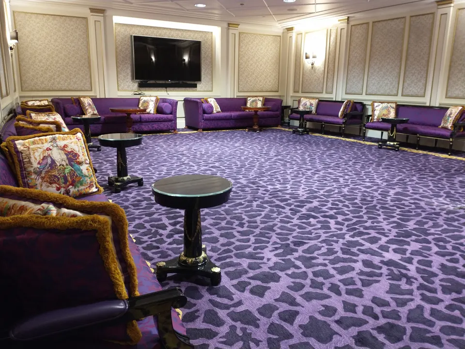 Fernseh- und Spielzimmer mit großem Wandbildschirm, violetten Sofas, kleinen runden Tischen und einem Teppich mit Leopardenmuster