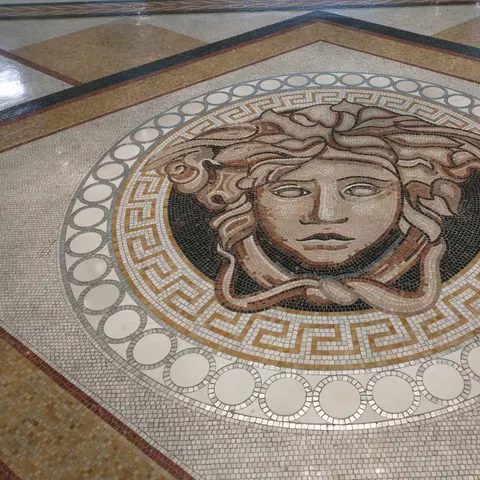 Medusa-Kopf als Bodenmosaik, umgeben von einem goldfarbenen Mäandermuster und kreisförmigen Ornamenten