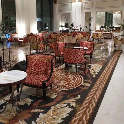 Mosaico-Lounge mit roten Sesseln, kleinen Tischen und einem Teppich mit großflächigen floralen Ornamenten