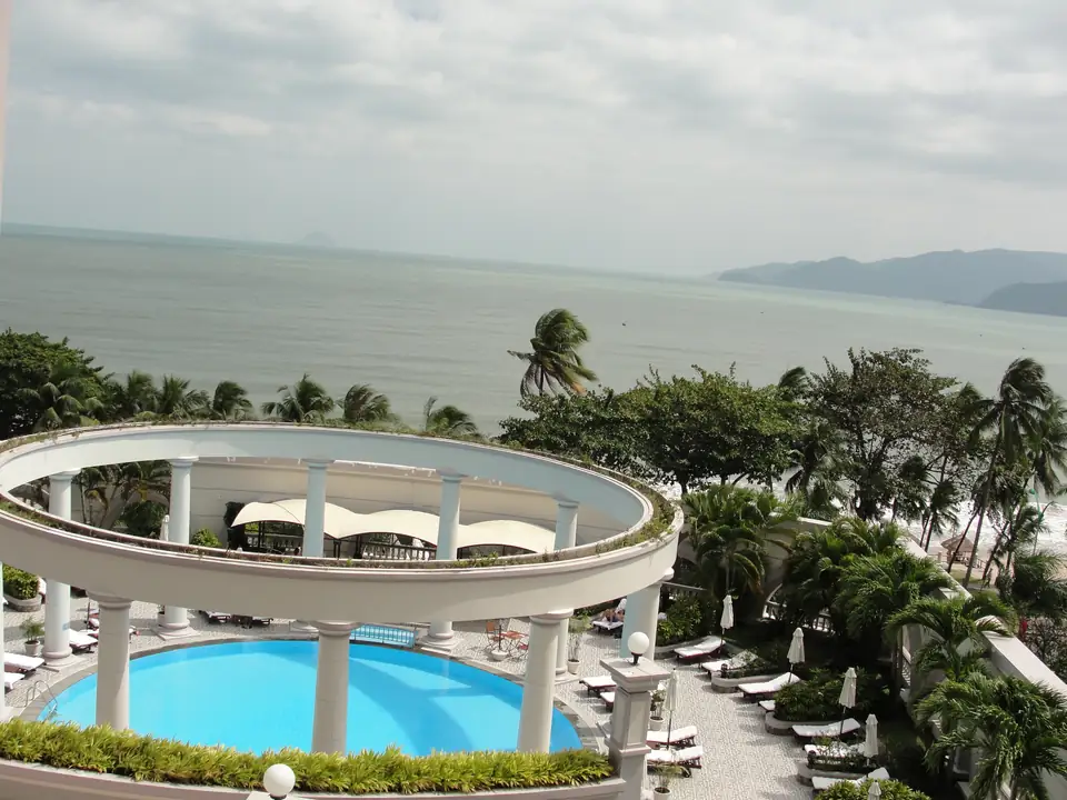 Runder Hotelpool mit weißem Säulengang, Palmen und Blick auf die Bucht von Nha Trang