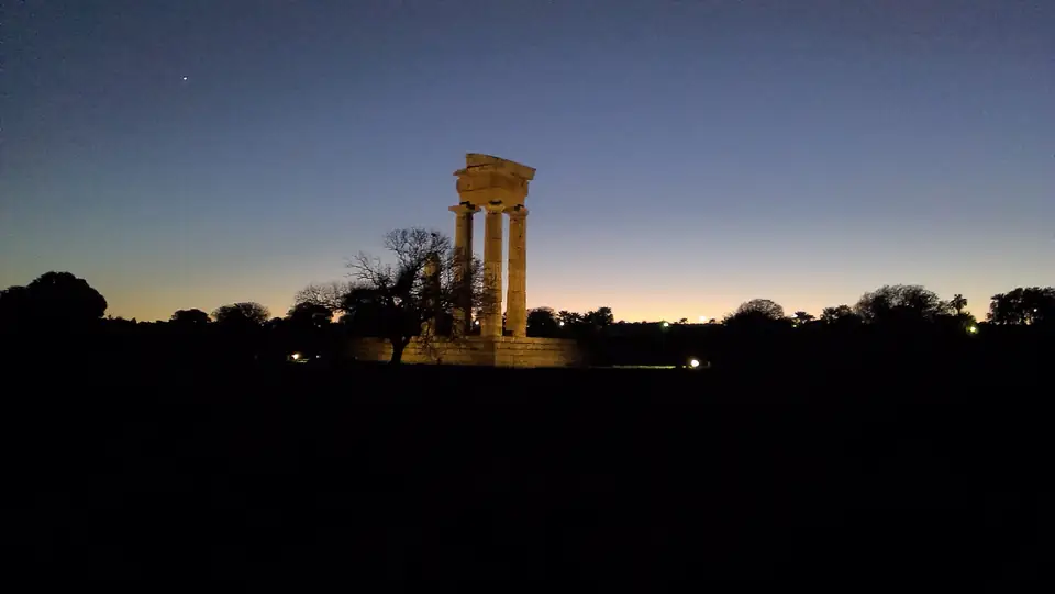 Beleuchtete antike Säulen vor Bäumen und einem Himmel in der Abenddämmerung